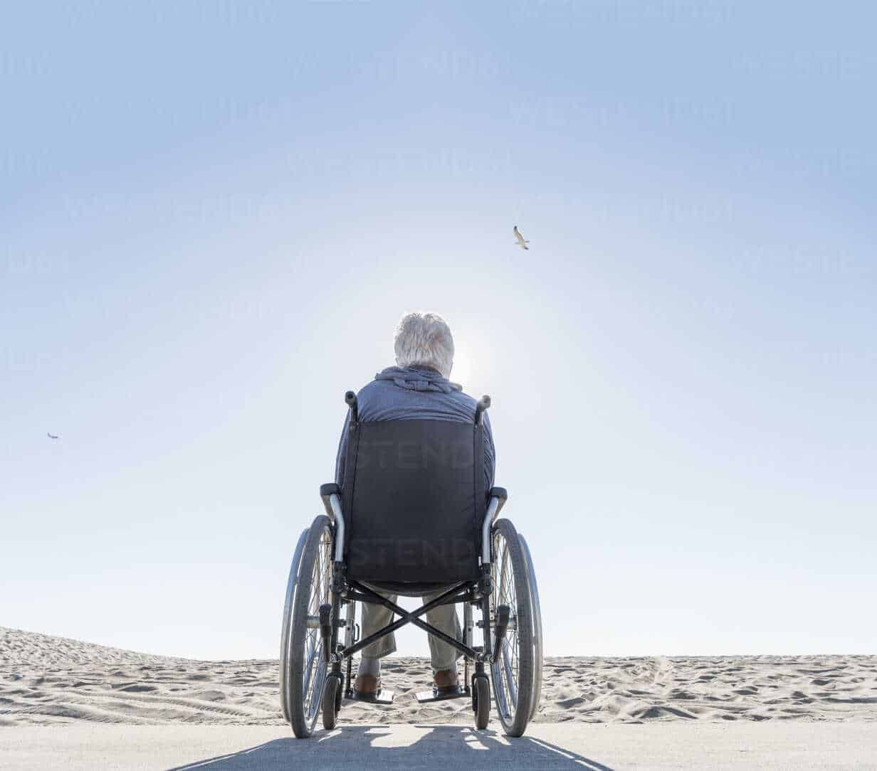 Rear view of senior man in wheelchair looking out from beach, Playa del ...